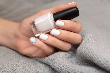 Female hand with white nail design holding nail polish bottle