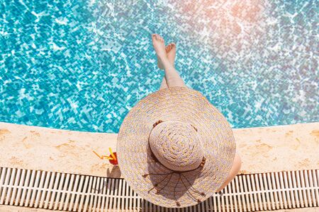 Young girl wearing sun hat siting by the pool with cocktail.
