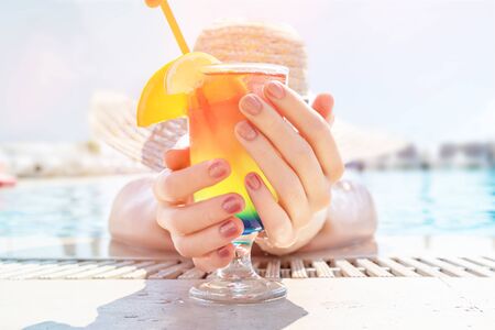 Young girl wearing sun hat siting by the pool with cocktail.の写真素材