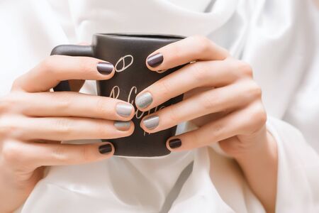 Female hands with glitter nail design holding black cupの写真素材