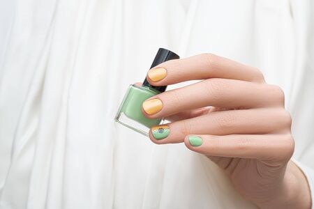 Green and yellow nail design. Female hand with green nail art holding green nail polish