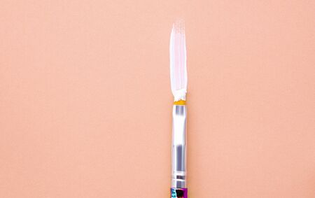 Paint brush with white acrylic paint on orange background