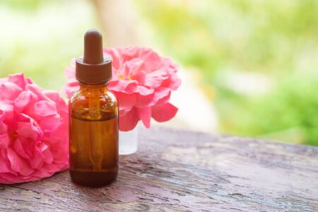Rose essential oil in a brown glass bottle with a rose flowers on background.の写真素材