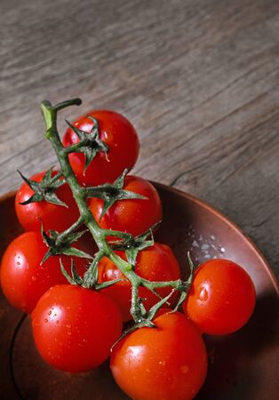 Fresh juicy ripe cherry tomatoes branch in a clay plate on a wooden desk.の写真素材