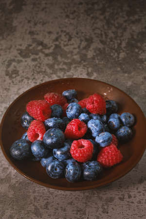 Blueberry and raspberry in a clay plate. Raw berries mix close up. Summer fresh berriesの写真素材