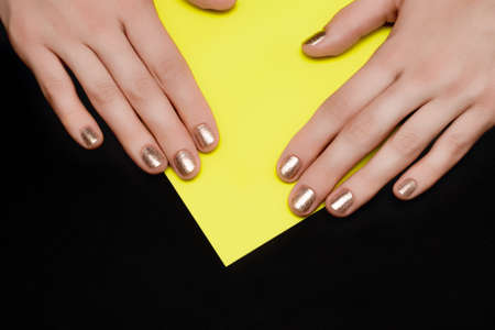 Female hands with golden nail design. Golden nail polish manicure. Female hands on yellow black backgroundの写真素材