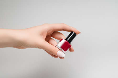 Female hand holding red nail polish bottle. Female hand with white nail designの写真素材