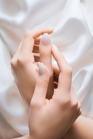 Female hands with white nail design. White glitter nail polish manicure. Woman hands on white fabric background.の写真素材