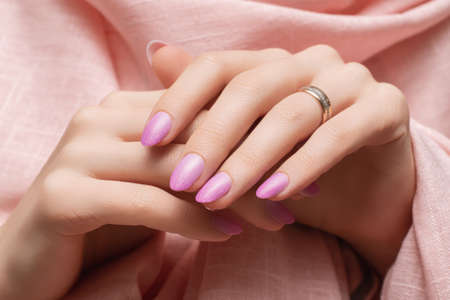 Female hands with pink nail design. Rose glitter nail polish manicure. Woman hands on rose fabric...