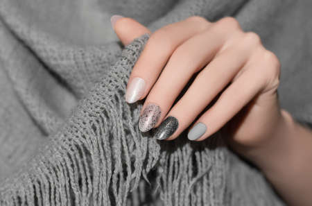 Female hands with glitter silver nail design. Silver nail polish manicure. Woman hands hold gray wool shawl.の写真素材