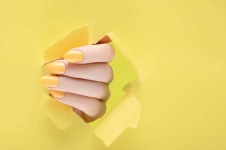 Female hand with yellow nail design. Yellow nail polish manicure. Color of the Year 2021 manicure on yellow backgroundの写真素材