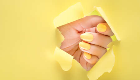 Female hand with yellow nail design. Glitter yellow nail polish manicure. Woman hand on yellow paper background.の写真素材