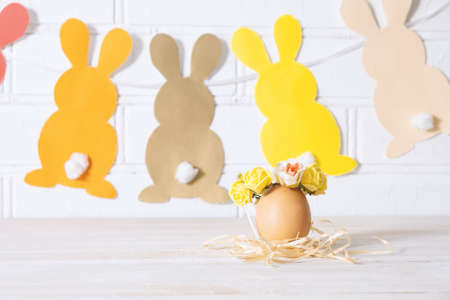 Easter egg in a basket. Easter egg decorated with yellow roses wreath and paper bunnies