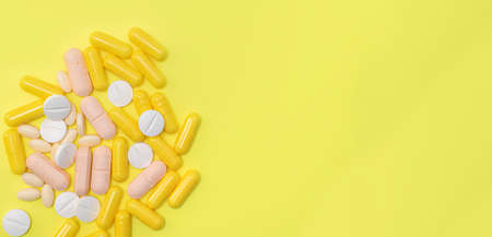 Assorted pharmaceutical medicine pills, tablets and capsules over yellow background.