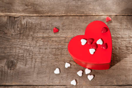 Valentine's Day gift box with red hearts candies. Heart shaped box decorated with candies and ribbons on wooden backgroundの写真素材