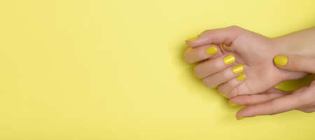 Female hands with yellow nail design. Glitter yellow nail polish manicure. Female hands on yellow background. copy space.の写真素材