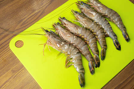 Fresh raw tiger prawns on yellow plastic cutting board. Raw seafood, raw shrimpsの写真素材