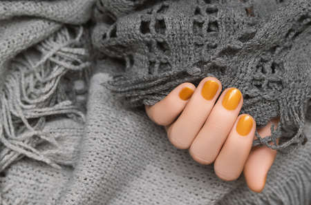 Female hand with yellow nail design. Glitter nail polish manicure. Woman hand on gray woolen backgroundの写真素材