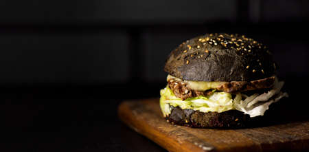 Beef burger with a black bun on a wooden desk. Dark beef burger on a dark background with copy space.の写真素材
