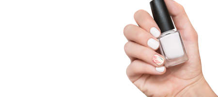 Female hand with white nail design holding nail polish bottle. Female hand on white background with copy spaceの写真素材
