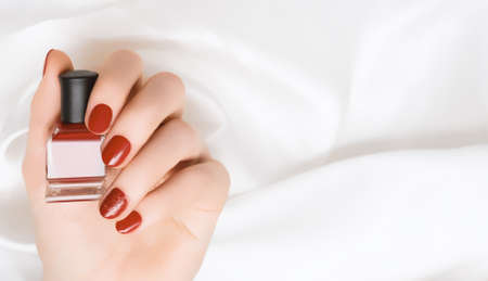 Female hand with red nail design. Red nail polish manicure. Woman hand hold red nail polish bottle....