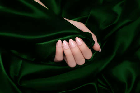 Female hand with pink nail design. Pink nail polish manicure. Woman hand on green fabric backgroundの写真素材