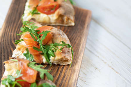 Roman pizza with salmon cut in pieces and served on a wooden board. Traditional roman pizza with...