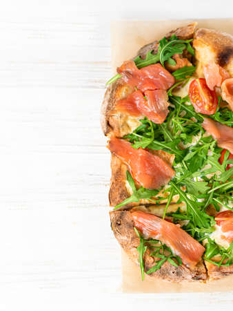 Roman pizza with salmon cut in pieces and served on a white wooden board. Traditional roman pizza with fishの写真素材