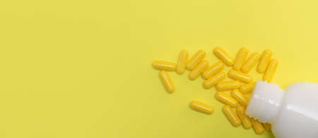 Yellow pharmaceutical medicine capsules over yellow background. White bottle with medical pills. copy spaceの写真素材