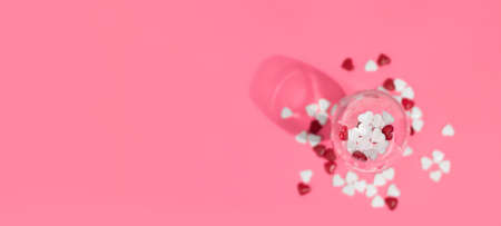 Heart shaped candies in glass top view. Valentine's day candies in champagne glass. Heart shaped candies on pink background. copy space.の写真素材