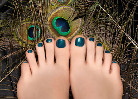Female feet with blue nail design. Female feet with peacock feather. Glitter blue nail polish pedicureの写真素材