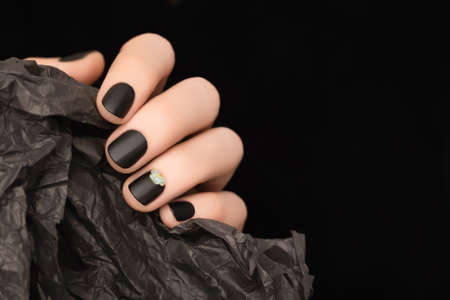 Female hand with black nail design. Black nail polish manicure. Woman hand hold wrinkled paper on black backgroundの写真素材