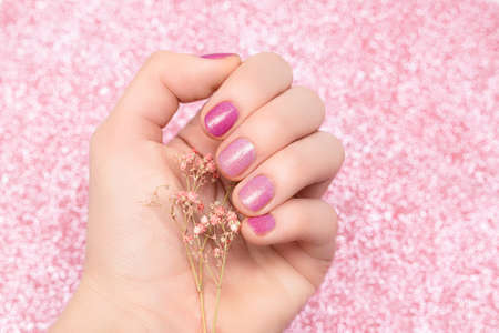Female hand with pink nail design. Glitter pink nail polish manicure. woman holding pink flower on glitter pink backgroundの写真素材