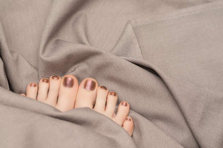 Female feet with beige nail design. Glitter beige nail polish pedicure on gray fabric backgroundの写真素材