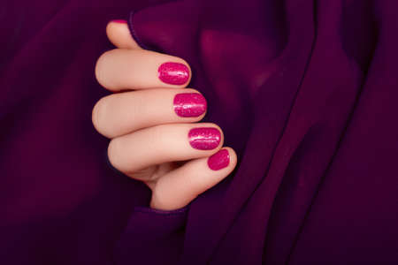 Female hand with pink nail design. Glitter pink nail polish manicure. Woman hand on purple fabric backgroundの写真素材