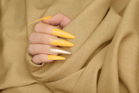 Female hand with yellow nail design. Long nail polish manicure. Woman hand on beige fabric backgroundの写真素材