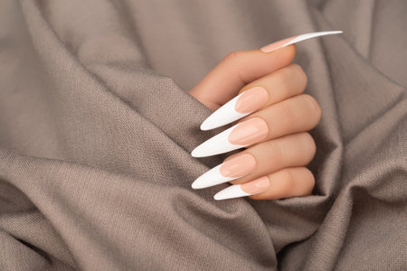 Female hand with long french nail design. Long french nail polish manicure. Woman hand on beige fabric backgroundの写真素材