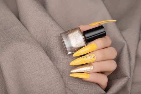 Female hand with yellow nail design. Long nail manicure. Woman hand with gold nail art hold gold nail polish bottle.の写真素材