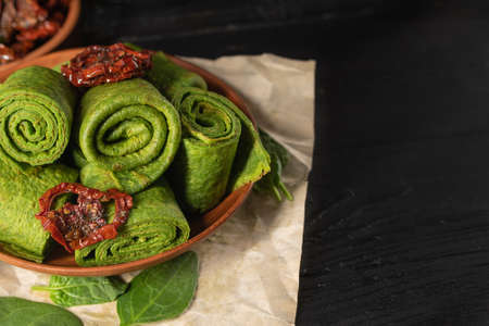 Vegetarian green pancakes decorated with dried tomato. Spinach pancakes in a brown plate on dark background. copy spaceの写真素材