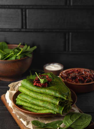 Vegetarian green pancakes decorated with dried tomatoes. Spinach pancakes in a brown plate on dark backgroundの写真素材