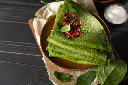 Vegetarian green pancakes decorated with dried tomatoes. Spinach pancakes in a brown plate on dark wooden backgroundの写真素材