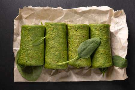 Vegetarian green pancake rolls breakfast. Spinach pancake rolls and spinach leaves on dark wooden...