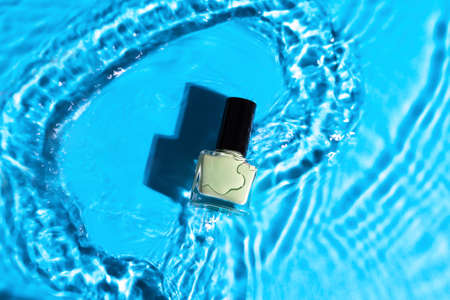Green nail polish bottle in blue water top shot. Nail polish bottle in clean waterの写真素材
