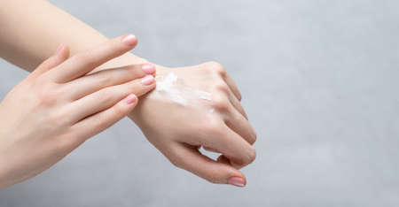 Beautiful young woman applying hand cream on gray background. Skincare cream on a female wrist