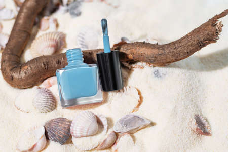 Blue nail polish bottle on a sand beach. Nail polish bottle on a summer sea sand background. Vacation nail polishの写真素材