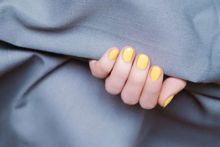 Female hand with yellow nail design. Glitter yellow nail polish manicure. Woman hand on blue fabric backgroundの写真素材