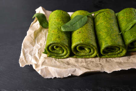 Vegetarian green pancakes. Spinach pancakes rolled up on a baking paper. Spinach vegetarian recipes