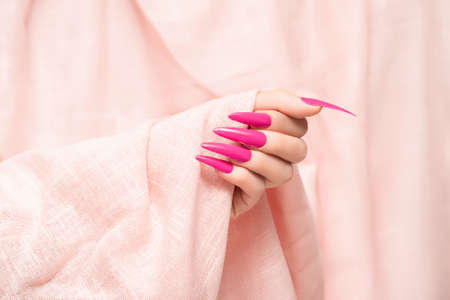 Female hand with pink stiletto nail design. Long nail polish manicure. Woman hand on glitter pink fabric background.の写真素材