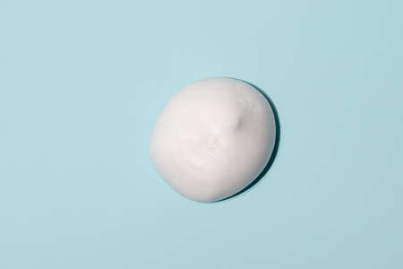 Drop of white beauty cream isolated on blue background. Smear face cream isolated. hand cream ob blue backgroundの写真素材