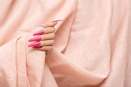 Female hand with pink stiletto nail design. Long nail polish manicure. Woman hand on rose fabric background.の写真素材